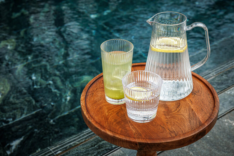 Stripe Pitcher 1,5 liter från Barcompagniet på ett träbord intill en pool. Serverad med citronvatten i matchande Stripe-glas – en elegant detalj för somriga stunder.