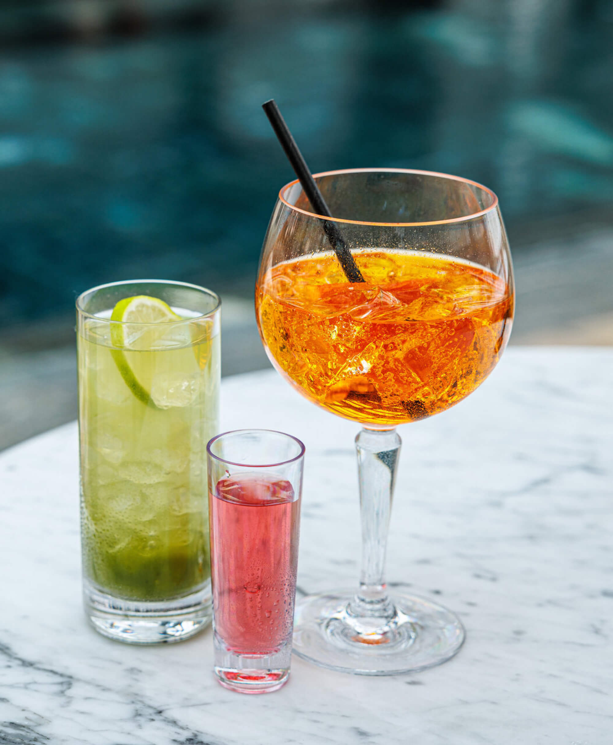 Okrossbara plastglas - Palma-kollektionen med orange spritz, grön limondryck och rosa shotglas på marmorunderlag<br />
